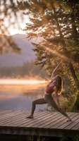 Young woman practicing yoga warrior pose on wooden dock at golden hour sunrise by mountain lake with pine trees creating peaceful outdoor fitness moment.
