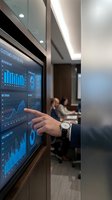 Businessman pointing at digital dashboard displaying analytics and customer metrics on interactive screen in modern office meeting room with colleagues.