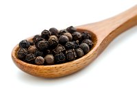 Black peppercorns in wooden spoon on white background, macro view of aromatic whole spices for cooking and seasoning food preparation.