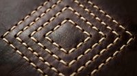 Brown leather surface with decorative diamond-shaped stitching pattern in contrasting thread creating geometric texture for luxury goods and craftsmanship.