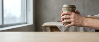 Male hands holding glass jar with savings money on wooden table near window in cozy home interior for financial planning and budget management concept.