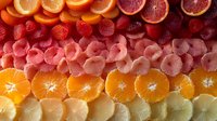 Fresh citrus fruit slices arranged in colorful rows including blood orange, grapefruit, orange, and lemon creating vibrant gradient pattern for food background.