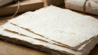 Handmade paper sheets with natural texture and deckled edges stacked on wooden surface for craft projects and artistic applications.