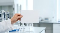 Scientist in white lab coat holding blank white card in modern laboratory with test tubes and equipment, suitable for research, healthcare, and corporate messaging.