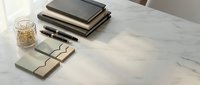Modern minimalist workspace with stacked notebooks, pens, and eyeglasses on white marble desk surface for professional office design and productivity concepts.