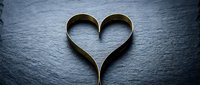 Golden heart shape formed by elegant curved metal bands on dark slate stone surface for romantic wedding anniversary celebration designs.