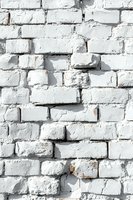Rough white painted brick wall with uneven surface texture and shadows creating depth. Old masonry background for urban and industrial design projects.