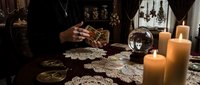 Fortune teller reading tarot cards with crystal ball and candles in mystical atmosphere. Spiritual guidance, divination and esoteric practices concept.