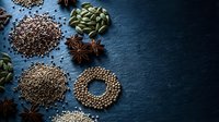 Assorted whole spices arranged on dark slate surface, including star anise, cardamom, coriander, and mustard seeds with copy space.
