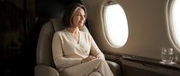 Elegant mature businesswoman in beige suit relaxing in luxury private jet cabin during flight, representing corporate travel and executive lifestyle.