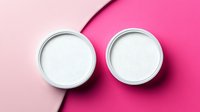 Two white round cosmetic jars on diagonal pink background with shadow casting minimal composition for beauty product presentation and skincare branding.