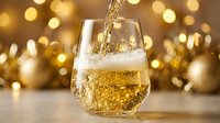 Golden beverage pouring into glass with sparkling bokeh lights and festive decorations in background, suitable for celebration and holiday marketing materials.