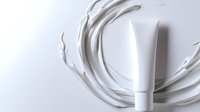 White cosmetic tube with dynamic cream splash swirl on light background, minimalist skincare product presentation for beauty and personal care advertising.