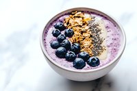 Purple smoothie bowl topped with fresh blueberries, granola and chia seeds on marble background, healthy breakfast concept for wellness lifestyle.