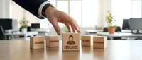 Business hand selecting employee wooden block from training, mentoring, healthcare, wellbeing options on office desk for human resources management.