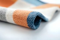 Rolled striped cotton fabric in orange, blue and white colors showing detailed textile weave texture and pattern on light background. Macro photography.
