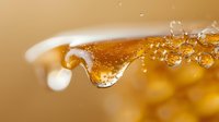 Golden honey drip with bubbles captured in macro photography against warm amber background, showcasing viscosity and natural sweetness in food photography.