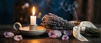 Aromatherapy spa setting with burning candle, dried lavender bundles, amethyst crystals and ribbon on wooden surface for relaxation and wellness rituals.