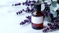 Essential oil brown glass bottle with blank label surrounded by fresh purple lavender flowers and eucalyptus leaves on light background for aromatherapy and spa.