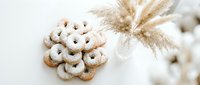 Traditional homemade vanilla crescent cookies dusted with powdered sugar arranged on white surface with dried pampas grass for festive holiday baking.