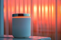 White cosmetic jar on table with soft orange sunset lighting through curtained window creates atmospheric mood for beauty product photography.