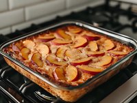 Fresh baked peach pie with sliced fruit arranged in rows on top of creamy custard filling in glass baking dish, golden brown crust on stovetop.