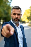 Confident mature businessman in navy suit jacket pointing directly at camera with assertive expression against blurred outdoor background.