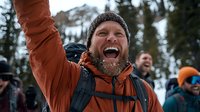 Joyful bearded Caucasian man in orange winter jacket and beanie celebrating outdoors with friends during snowy mountain adventure, expressing pure excitement and happiness.