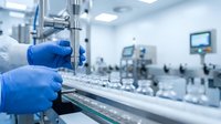Pharmaceutical manufacturing worker in blue gloves operating precision equipment in sterile cleanroom facility for drug production and quality control testing.