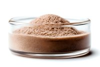Brown powder supplement in glass petri dish against white background, macro photography showing texture and detail of nutritional or protein powder supplement.