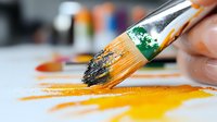 Paint brush with orange and green paint strokes on white surface, macro photography showing artistic texture and creative process in painting studio.