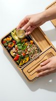 Person with light skin tone holding wooden lunch box with compartments containing roasted vegetables, grains, and dressing, promoting healthy meal prep and nutrition.