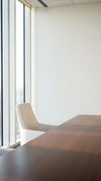 Modern minimalist office interior with wooden conference table and white chair by large windows for corporate meeting spaces.