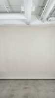 Empty white wall in modern industrial loft space with exposed ceiling pipes and concrete floor for creative projects and exhibitions.