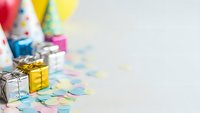 Colorful birthday party supplies with wrapped gifts, party hats and confetti on white background. Celebration decoration elements for festive events.