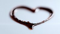 Dark liquid heart shape formed on light surface with tiny droplets and reflective sheen, creating romantic minimalist composition for Valentine's designs.