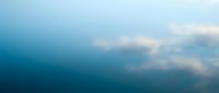 Serene blue water surface with soft white clouds reflecting, creating peaceful aquatic mirror effect for meditation and wellness content.