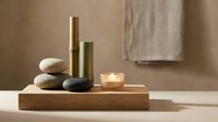 Zen spa composition with stacked stones, bamboo tubes and glowing candle on wooden tray creating peaceful meditation atmosphere for wellness relaxation.