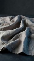 Soft beige linen fabric with natural wrinkles and folds creating organic texture patterns on dark surface for home decor and textile design projects.