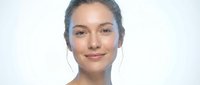 Young mixed-race woman with natural makeup and pulled-back hair smiling warmly at camera against clean white background for lifestyle and beauty content.