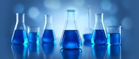 Laboratory glassware with blue chemical solutions on reflective surface. Scientific research equipment including beakers, flasks and test tubes for experiments.