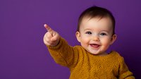 Happy baby in mustard yellow knit sweater pointing and laughing against purple background, showing joy and curiosity. Studio portrait capturing genuine childhood emotion.