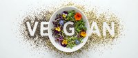 Vegan lettering made from seeds with a bowl of fresh microgreens and edible flowers on white background, promoting plant-based healthy lifestyle.