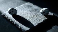 Two smooth river stones placed on rough textured slate surface creating dramatic shadows in monochrome composition for zen meditation and spa concepts.