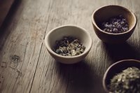 Aromatic dried herbs and spices in rustic ceramic bowls on weathered wooden surface, moody natural lighting creates atmospheric composition for culinary concepts.
