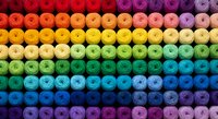 Colorful embroidery thread spools arranged in rainbow gradient pattern from red to purple. Craft supplies for sewing, needlework and textile projects.