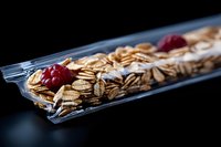 Crunchy granola bar with fresh raspberries and oat flakes in transparent packaging on dark background, macro food photography for healthy snack advertising.