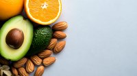 Fresh halved orange, ripe avocado, and scattered almonds on light background, showcasing healthy fats and vitamin C rich ingredients for nutritious eating and food design.