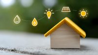 Small white house model with golden roof and illustrated sustainable energy icons showing water drops, lightbulb and solar panel against blurred green background.