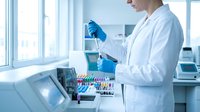 Female scientist in white lab coat using pipette for sample analysis in modern laboratory with test tubes and equipment.